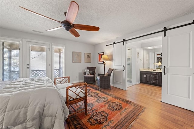 bedroom with connected bathroom, access to exterior, a textured ceiling, a barn door, and light hardwood / wood-style floors