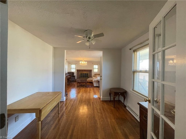 hall with a textured ceiling, a baseboard heating unit, wood finished floors, baseboards, and an inviting chandelier