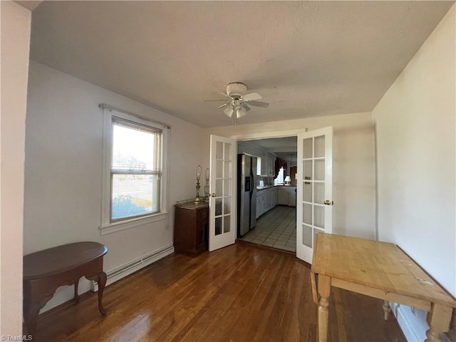 unfurnished dining area with a ceiling fan, baseboard heating, dark wood-style flooring, and french doors