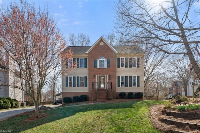 colonial-style house with a front yard, cooling unit, and brick siding