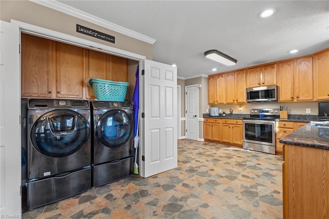 kitchen with washing machine and clothes dryer, ornamental molding, stainless steel appliances, stone finish floor, and a textured ceiling