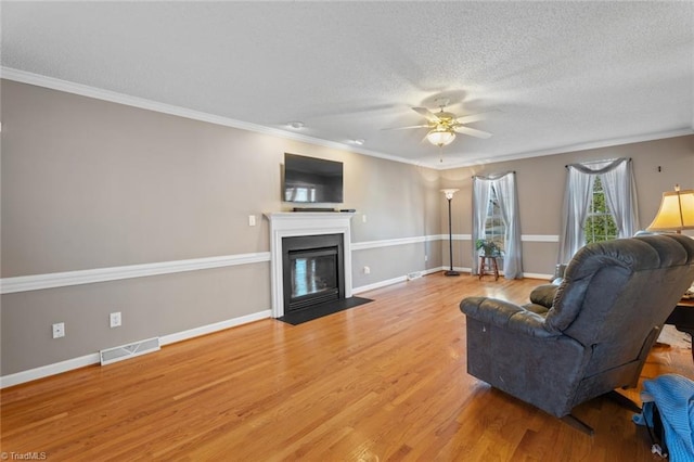 living room with visible vents, a fireplace with flush hearth, light wood-type flooring, a textured ceiling, and a ceiling fan