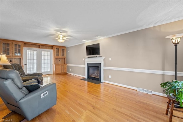 living room featuring visible vents, a fireplace with flush hearth, ceiling fan, light wood-style floors, and a textured ceiling