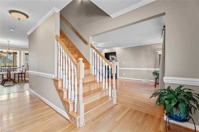 stairway with wood finished floors, baseboards, ornamental molding, a textured ceiling, and a chandelier