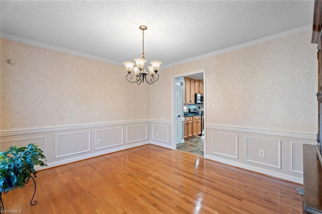 unfurnished room with wood finished floors, a textured ceiling, a chandelier, and ornamental molding