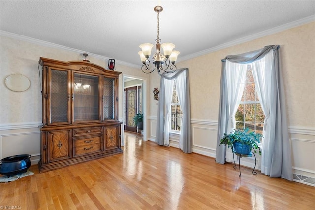 dining room featuring ornamental molding, a healthy amount of sunlight, light wood-type flooring, and a chandelier