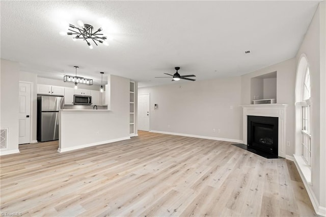 unfurnished living room with a textured ceiling, light hardwood / wood-style floors, and ceiling fan