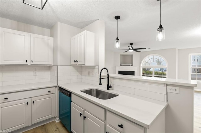 kitchen with sink, white cabinetry, hanging light fixtures, dishwashing machine, and kitchen peninsula