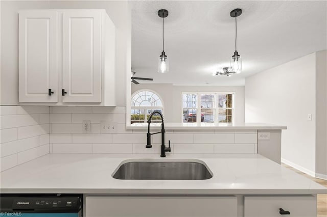 kitchen with pendant lighting, sink, dishwasher, light stone countertops, and white cabinets