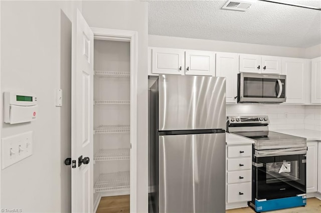 kitchen with light hardwood / wood-style flooring, appliances with stainless steel finishes, white cabinetry, tasteful backsplash, and a textured ceiling