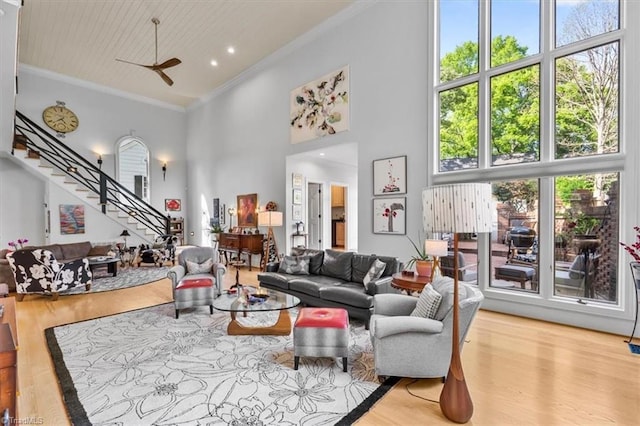 living room featuring crown molding, a high ceiling, ceiling fan, wood finished floors, and stairway