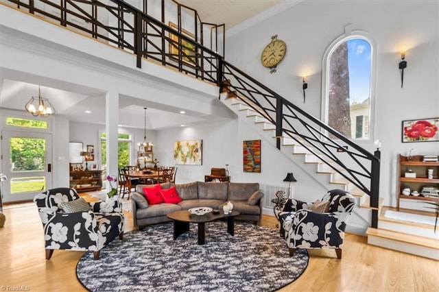living area featuring wood finished floors, a high ceiling, a chandelier, ornamental molding, and stairs
