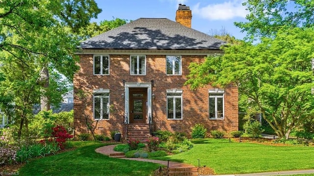 view of front facade with brick siding, a front lawn, and a chimney
