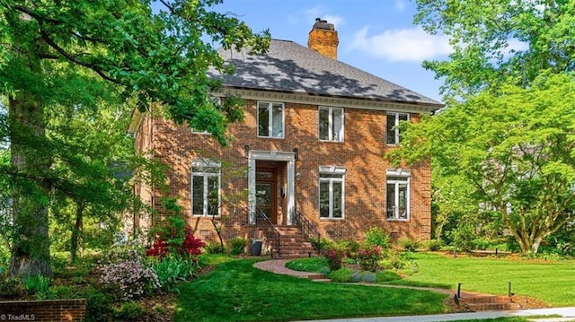 back of house featuring a chimney, a yard, and brick siding