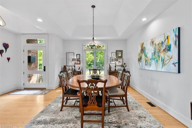 dining room featuring light wood-style floors, a raised ceiling, baseboards, and visible vents
