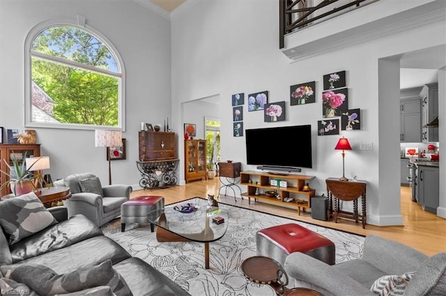 living room with crown molding, baseboards, light wood-style flooring, and a towering ceiling