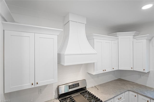 kitchen featuring stainless steel stove, custom range hood, decorative backsplash, and white cabinetry