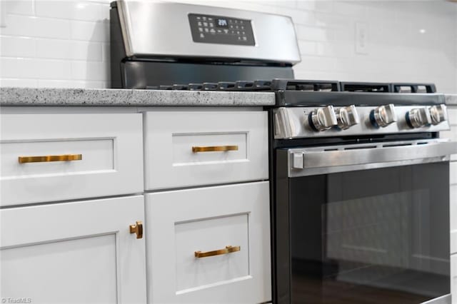 kitchen with white cabinetry, light stone counters, backsplash, and gas stove