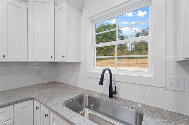 kitchen with white cabinets, light stone countertops, sink, and decorative backsplash