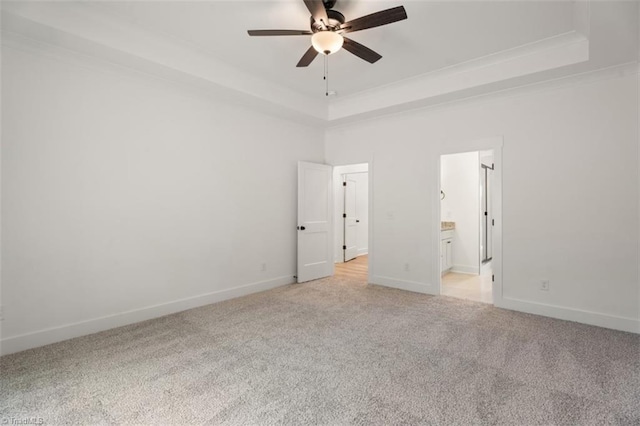 unfurnished bedroom with ceiling fan, ensuite bath, light carpet, and a tray ceiling