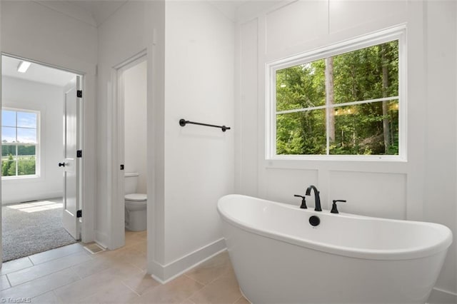 bathroom featuring tile patterned floors, a bath, a healthy amount of sunlight, and toilet