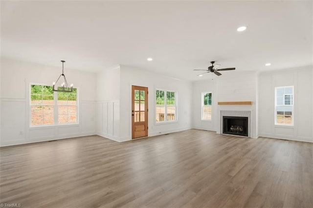 unfurnished living room featuring wood-type flooring, a healthy amount of sunlight, a tile fireplace, and ceiling fan with notable chandelier