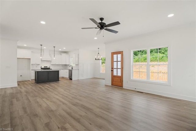 unfurnished living room with ceiling fan with notable chandelier, sink, and light wood-type flooring