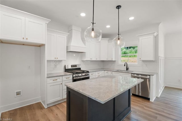 kitchen with premium range hood, stainless steel appliances, a kitchen island, white cabinetry, and light hardwood / wood-style flooring