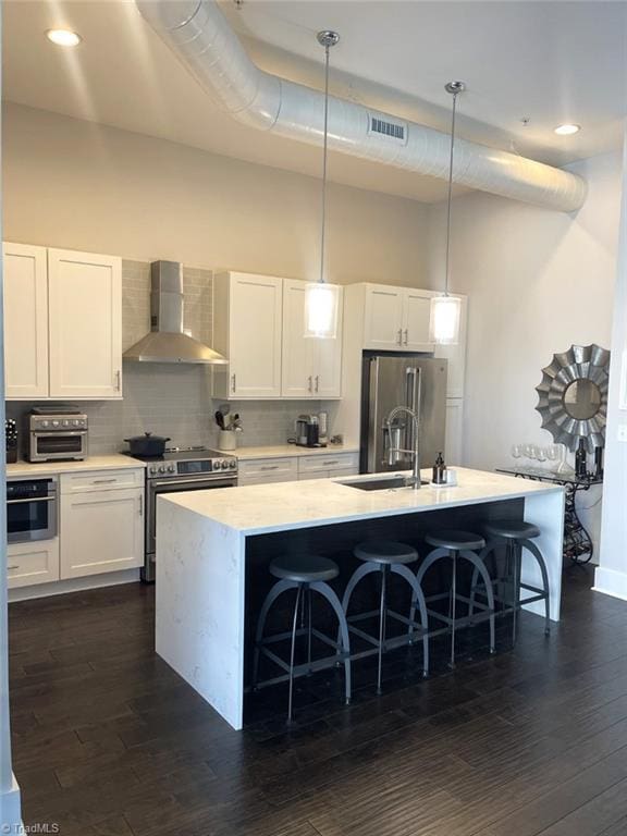 kitchen featuring appliances with stainless steel finishes, wall chimney exhaust hood, a towering ceiling, visible vents, and a center island with sink