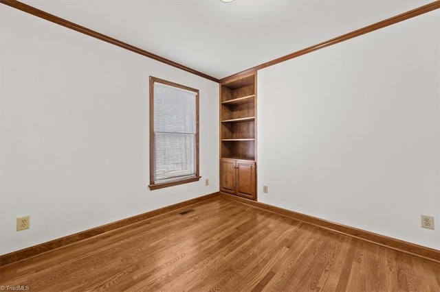 empty room featuring baseboards, visible vents, built in features, ornamental molding, and light wood-style floors