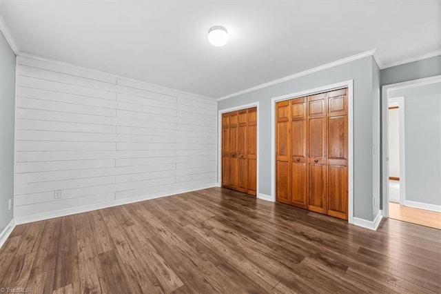 unfurnished bedroom with crown molding, dark wood-type flooring, baseboards, and multiple closets