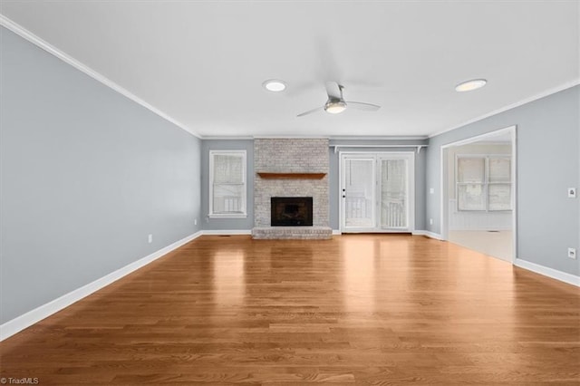 unfurnished living room featuring ceiling fan, ornamental molding, a brick fireplace, and wood finished floors