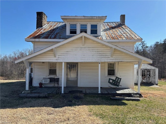 view of front of house featuring a front yard, a porch, a chimney, and a standing seam roof