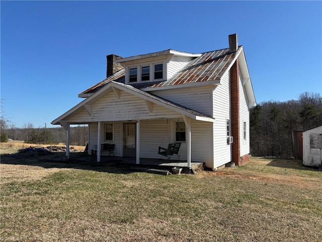 view of front of house with a porch, a chimney, a front yard, and metal roof