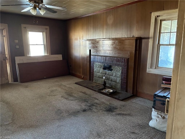 unfurnished living room with ceiling fan, carpet, wood walls, and a fireplace