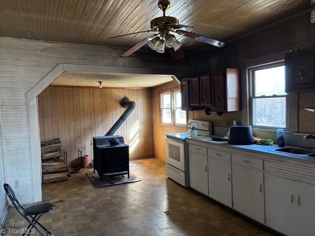 kitchen featuring wooden walls, white range with electric cooktop, a wood stove, plenty of natural light, and a sink