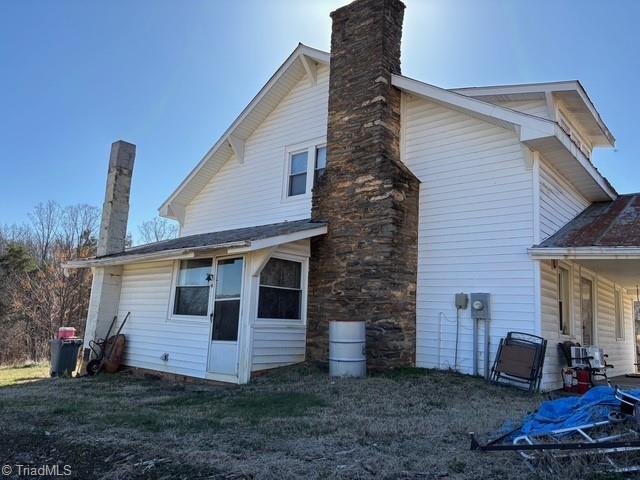 back of house featuring a lawn and a chimney