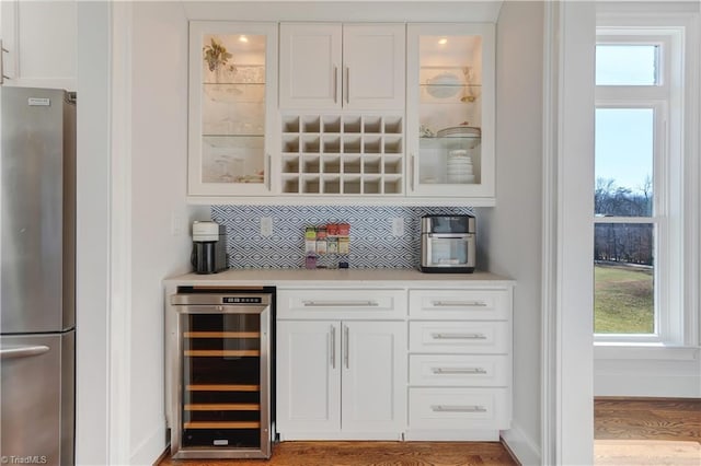 bar featuring freestanding refrigerator, beverage cooler, backsplash, and baseboards