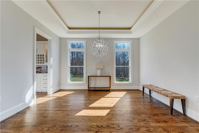 unfurnished dining area featuring a tray ceiling, a healthy amount of sunlight, an inviting chandelier, and wood finished floors