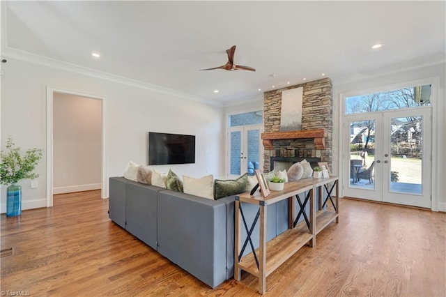 living room with french doors, crown molding, a stone fireplace, and wood finished floors