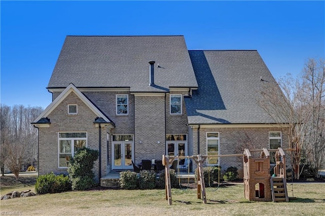 rear view of house featuring a playground, brick siding, a yard, french doors, and roof with shingles