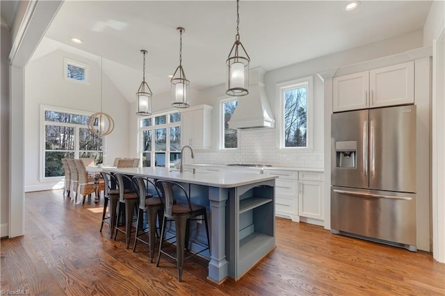 kitchen featuring an island with sink, wood finished floors, custom exhaust hood, white cabinetry, and stainless steel refrigerator with ice dispenser