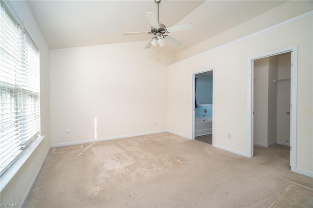 unfurnished bedroom featuring lofted ceiling, ensuite bathroom, carpet, baseboards, and a spacious closet