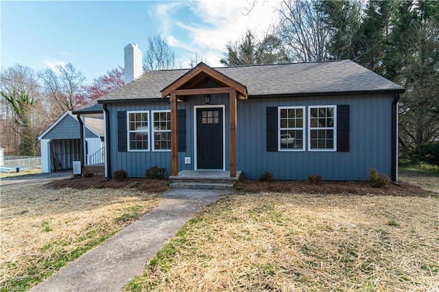 bungalow-style home featuring a front yard, a carport, a chimney, and a shingled roof