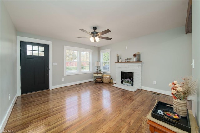 unfurnished living room with a brick fireplace, a ceiling fan, baseboards, and light wood finished floors