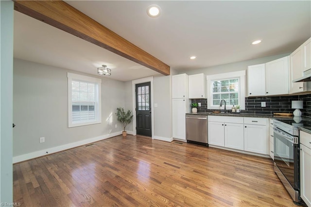 kitchen with beam ceiling, a sink, dark countertops, appliances with stainless steel finishes, and decorative backsplash