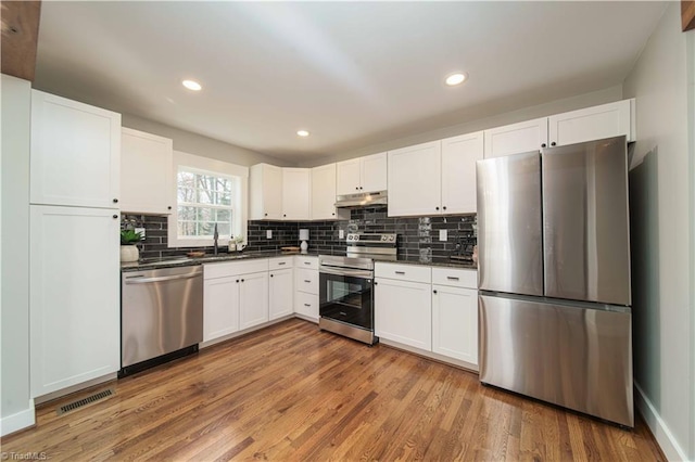 kitchen featuring light wood finished floors, visible vents, dark countertops, under cabinet range hood, and appliances with stainless steel finishes