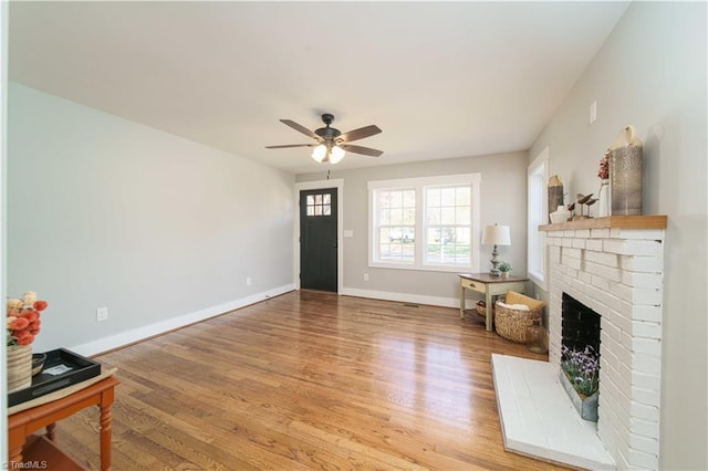 living area featuring a brick fireplace, wood finished floors, baseboards, and ceiling fan