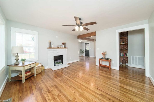 living room featuring baseboards, visible vents, a fireplace, ceiling fan, and light wood-style floors