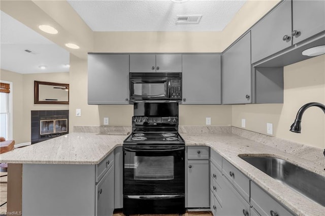 kitchen featuring a peninsula, black appliances, gray cabinets, and a sink